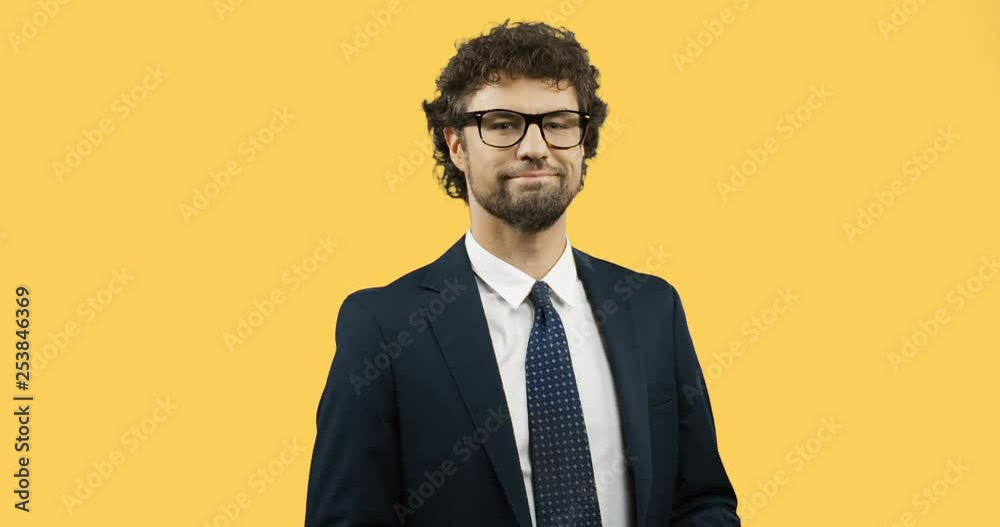 Portrait shot of the handsome succesful man in the glasses, suit and tie posing in front of the camera and tossing keys up like showing off. Yellow background screen. Portrait shot of the handsome succesful man in the glasses, suit and tie posing in front of the camera and tossing keys up like showing off. Yellow background screen.
