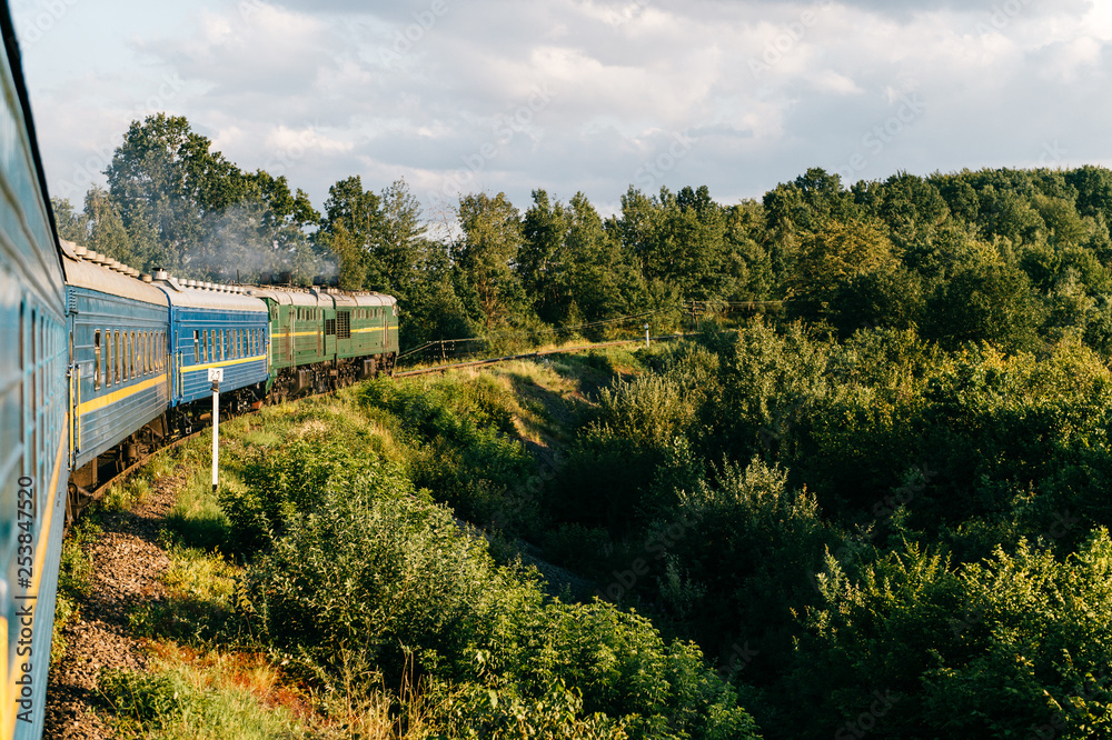 Landscape beautiful view out of window from riding train among summer nature with hills, mountains and forest. Vacation and travel concept. Locomotive with train cars moving along railroad track.