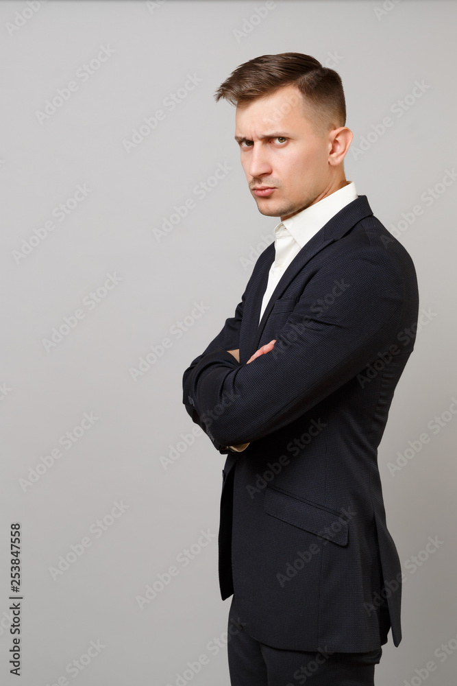 Side view of displeased young business man in classic black suit, shirt holding hands folded isolated on grey wall background in studio. Achievement career wealth business concept. Mock up copy space. Side view of displeased young business man in classic black suit, shirt holding hands folded isolated on grey wall background in studio. Achievement career wealth business concept. Mock up copy space.
