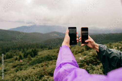 Unrecognizable travelers hands with smartphones take picture of fabulous nature landscape view in summer rainy day. Unknown tourists in camping adventure take selfie with cellphones. Happy moments. photo