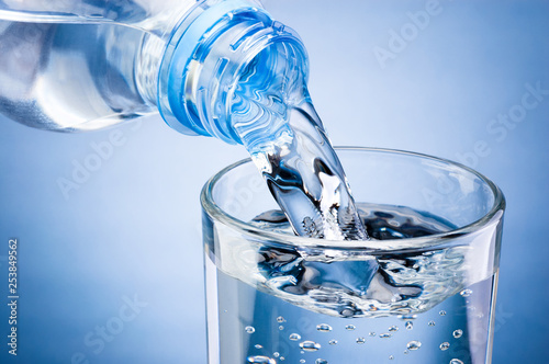 Pouring water from bottle into glass on blue background photo