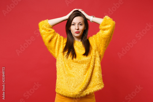 Portrait of serious confident young woman in yellow fur sweater putting hands on head isolated on bright red wall background in studio. People sincere emotions, lifestyle concept. Mock up copy space. © ViDi Studio