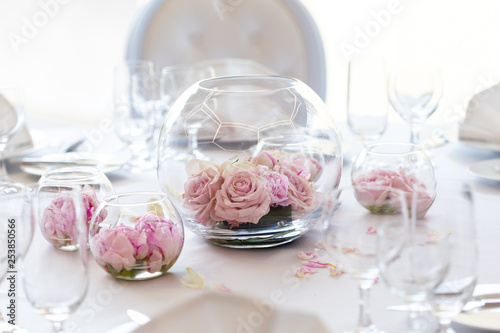 Detail of white wedding table set-up with fresh pink roses in glass bowls and rose petals. Blurry background. © Moving Moment