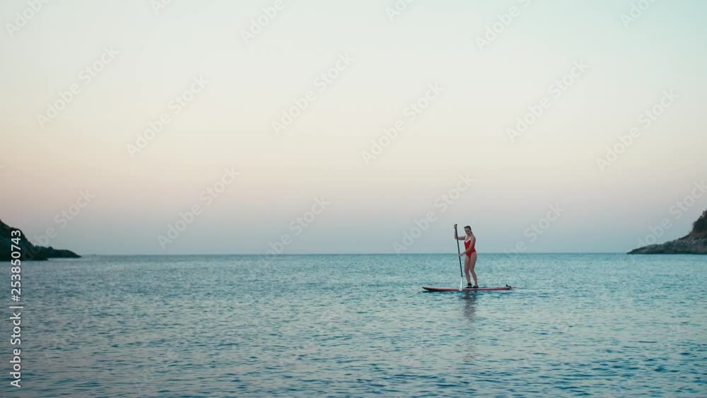 Woman in red swimsuit on SUP stand up paddle board on a bay at sunset. Woman in red swimsuit on SUP stand up paddle board on a bay at sunset.