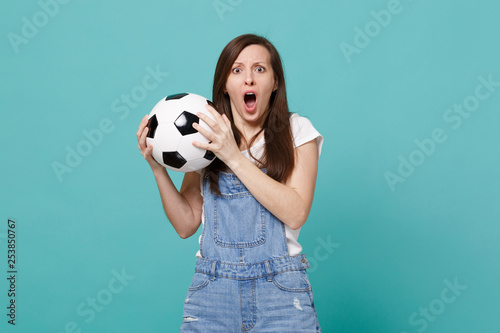 Shocked scared young woman football fan support favorite team with soccer ball keeping mouth wide open isolated on blue turquoise background. People emotions, sport family leisure lifestyle concept. © ViDi Studio