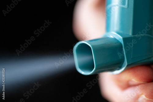 Hand holding blue asthma inhaler with spray coming out on black background. photo