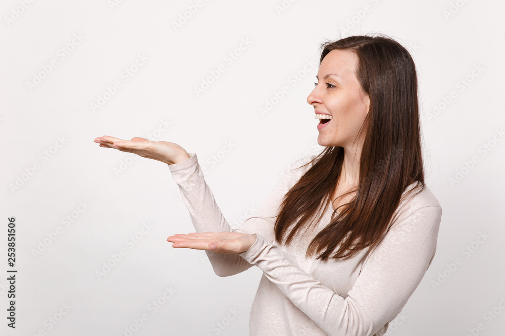 Portrait of laughing cheerful young woman in light clothes looking and pointing hands aside isolated on white wall background in studio. People sincere emotions, lifestyle concept. Mock up copy space. Portrait of laughing cheerful young woman in light clothes looking and pointing hands aside isolated on white wall background in studio. People sincere emotions, lifestyle concept. Mock up copy space.
