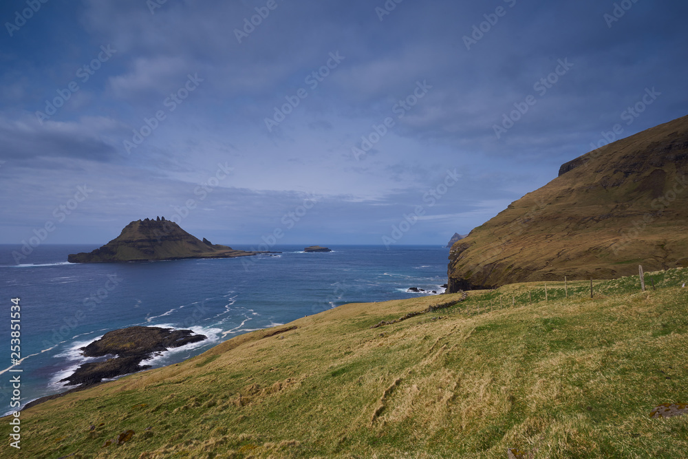 Epic colorful landscape of wild nordic or scandinavian coastline without trees with atlantic ocean, mountains, high cliffs in island Vagar in Faroe island taken in sunny, cloudy and windy summer day.