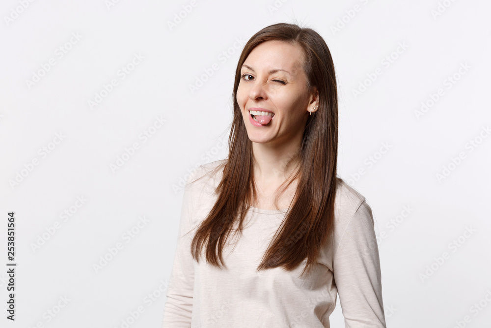 Portrait of funny cheerful blinking pretty young woman in light clothes showing tongue isolated on white wall background in studio. People sincere emotions, lifestyle concept. Mock up copy space. Portrait of funny cheerful blinking pretty young woman in light clothes showing tongue isolated on white wall background in studio. People sincere emotions, lifestyle concept. Mock up copy space.
