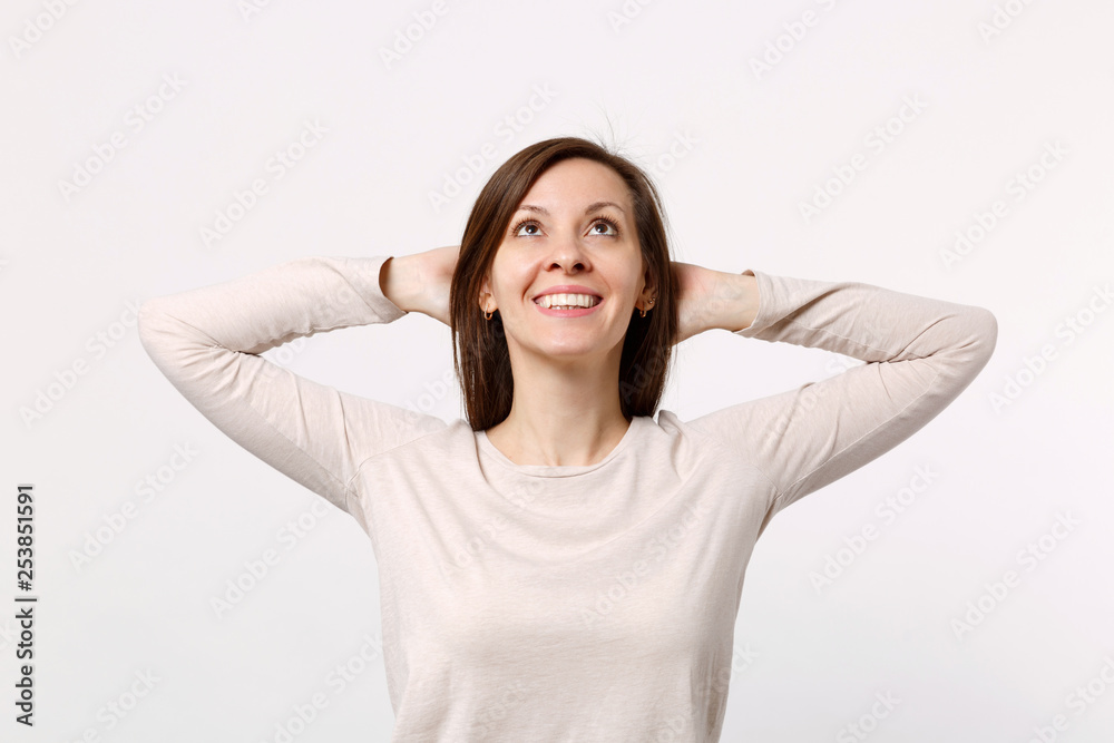 Portrait of smiling cute young woman in light clothes looking up, holding hands behind head isolated on white wall background in studio. People sincere emotions, lifestyle concept. Mock up copy space. Portrait of smiling cute young woman in light clothes looking up, holding hands behind head isolated on white wall background in studio. People sincere emotions, lifestyle concept. Mock up copy space.