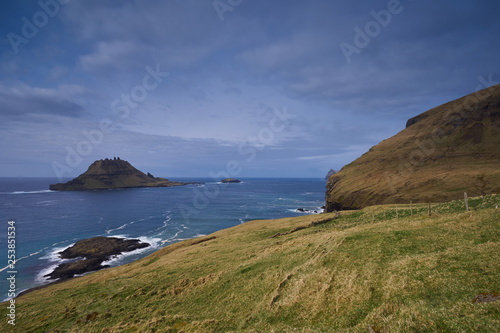 Epic colorful landscape of wild nordic or scandinavian coastline without trees with atlantic ocean, mountains, high cliffs in island Vagar in Faroe island taken in sunny, cloudy and windy summer day.