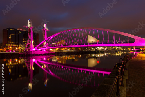 A night view of a pink neon arch bridge over a canal