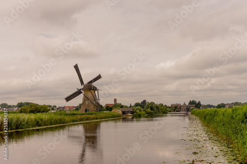 Netherlands, Rotterdam, Kinderdijk, heritage windmill above lush green grass along a canal © SkandaRamana