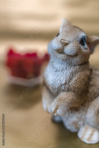 Young easter bunny, dressed in pink, sits in front of a bunch of red berries on a gold background