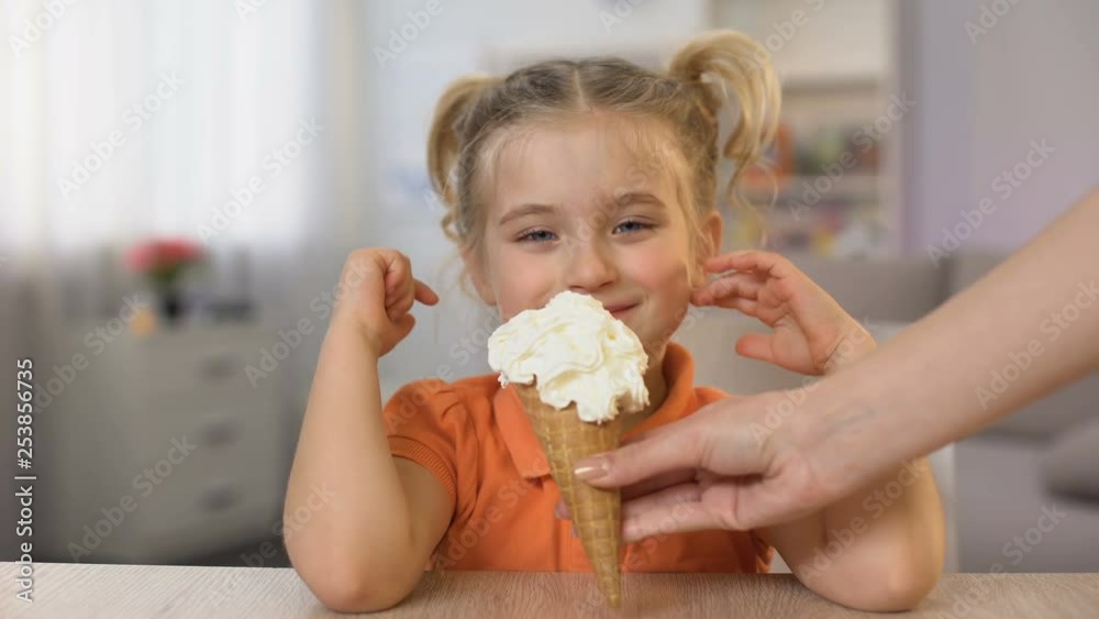 Cute girl tasting ice-cream cone from female hand, childhood surprise, snack Cute girl tasting ice-cream cone from female hand, childhood surprise, snack