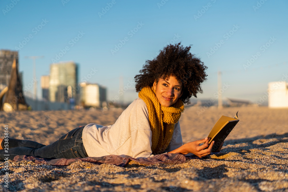 Woman lying in the sand, relaxing on the beach, reading a book Woman lying in the sand, relaxing on the beach, reading a book