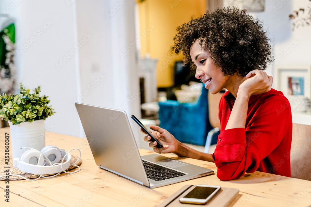 Smiling woman using laptop and cell phone at table