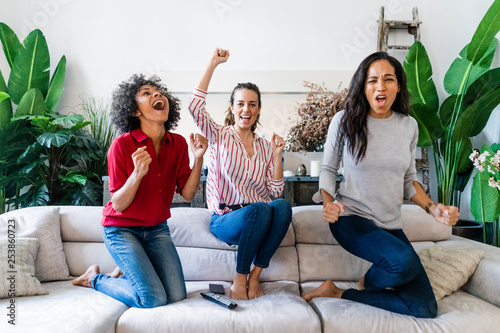 Three excited women on couch at home watching Tv and cheering photo
