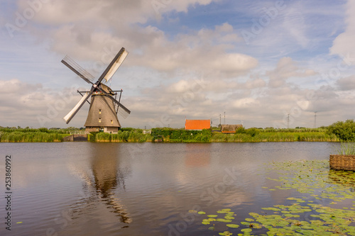 Netherlands, Rotterdam, Kinderdijk, heritage windmill above lush green grass along a canal with reflection