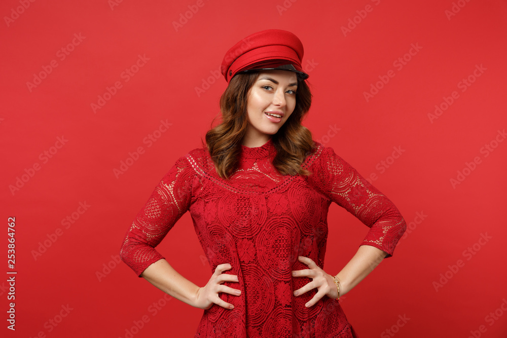 Portrait of attractive young woman in lace dress, cap looking camera standing with arms akimbo isolated on red wall background in studio. People sincere emotions lifestyle concept. Mock up copy space.