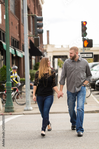 Attractive young couple holding hands crossing urban street