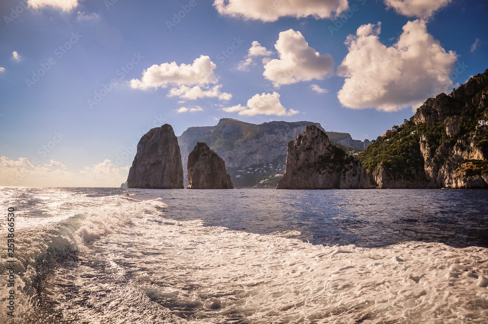 The Faraglioni of Capri seen from the sea, behind the wake of a boat, Italy