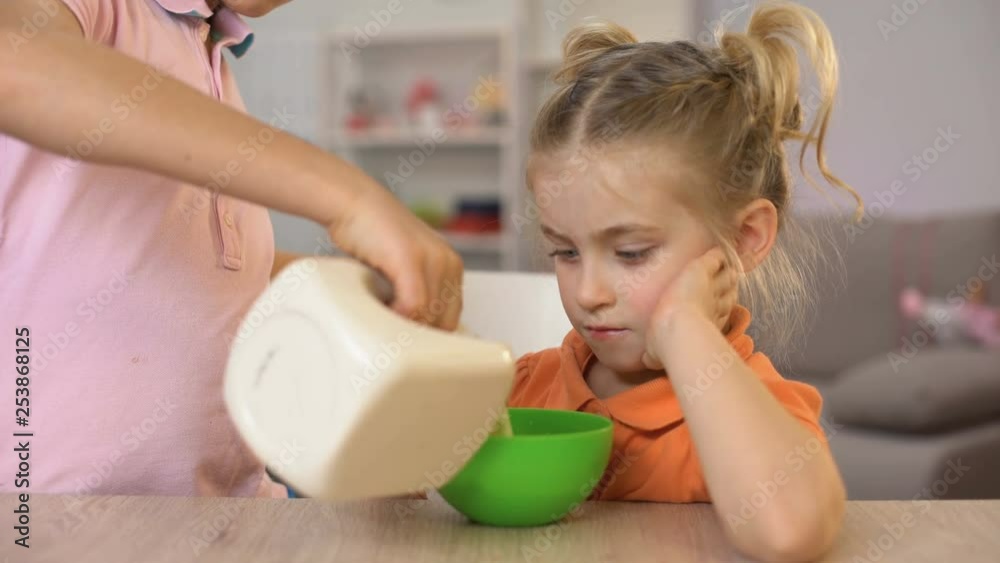 Brother pouring milk in cornflakes bowl, taking care of sister, family love Brother pouring milk in cornflakes bowl, taking care of sister, family love