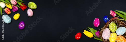 Panel kuchenny z motywem Colorful happy easter eggs in bird nest and tulips on dark empty slate stone blackboard wide panorama background with copy space design pattern 