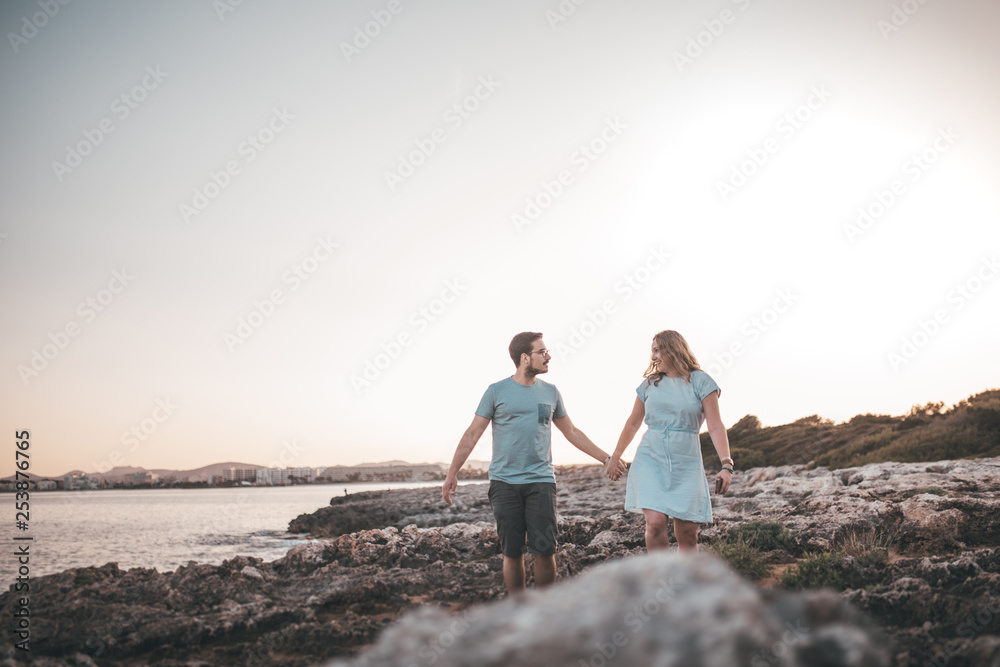 Paar spaziert über Felsen am Strand bei Sonnenuntergang