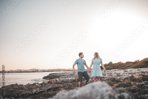 Paar spaziert über Felsen am Strand bei Sonnenuntergang