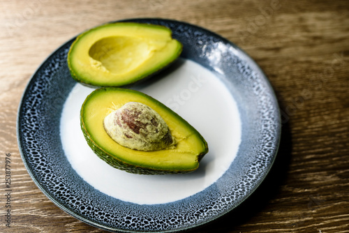 Avocado cut into half on a plate, wooden background