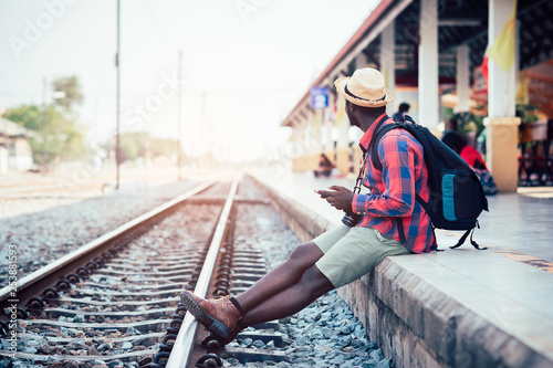 African man traveler playing smartphone waiting for the train on railroad station