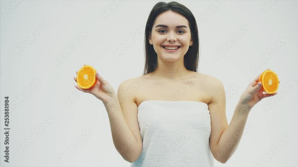 Happy young girl poses with fruit. During this she looks into the camera. Holds two pieces of orange in his hands and smiles. Happy young girl poses with fruit. During this she looks into the camera. Holds two pieces of orange in his hands and smiles.