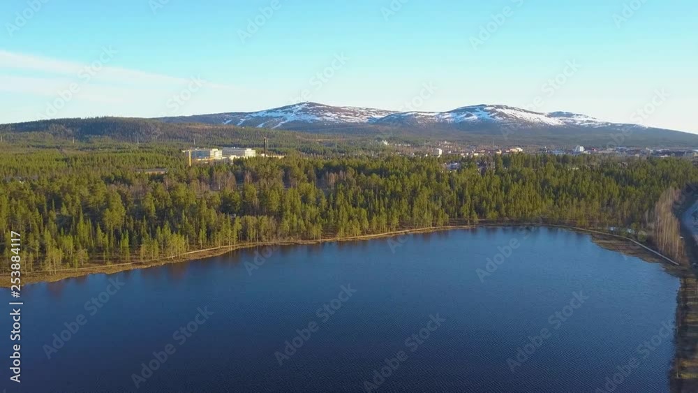 Aerial, tracking, drone shot, of a tornetrask lake, forest, a town and snowy, fell mountains, in the background, Swedish wilderness, on a sunny, spring day, in Abisko, Kiruna, Lapland, North Sweden Aerial, tracking, drone shot, of a tornetrask lake, forest, a town and snowy, fell mountains, in the background, Swedish wilderness, on a sunny, spring day, in Abisko, Kiruna, Lapland, North Sweden