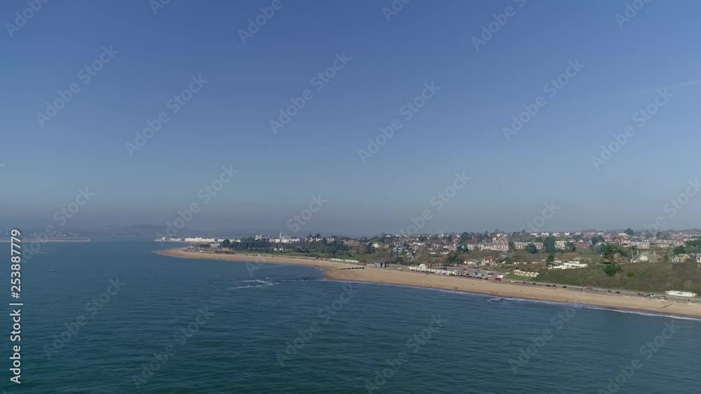 Wide aerial out a sea looking across Exmouth Beach. Some of the town surrounding the beach is visible, along with Dawlish Warren to the left of shot. Hazy and sunny. Wide aerial out a sea looking across Exmouth Beach. Some of the town surrounding the beach is visible, along with Dawlish Warren to the left of shot. Hazy and sunny.