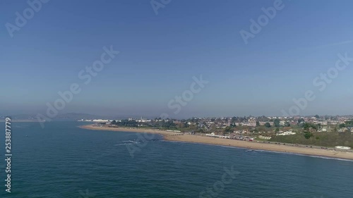 Wide aerial out a sea looking across Exmouth Beach. Some of the town surrounding the beach is visible, along with Dawlish Warren to the left of shot. Hazy and sunny. photo