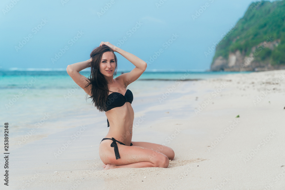Sexy tanned girl in black swimsuit posing on sandy beach near ocean. Beautiful model sunbathes and rests Sexy tanned girl in black swimsuit posing on sandy beach near ocean. Beautiful model sunbathes and rests