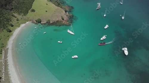 A top down aerial drone shot that slowly pivots around a fleet of anchored boats moored in a tropical paradise with a white sandy beach and crystal clear ocean waters. photo