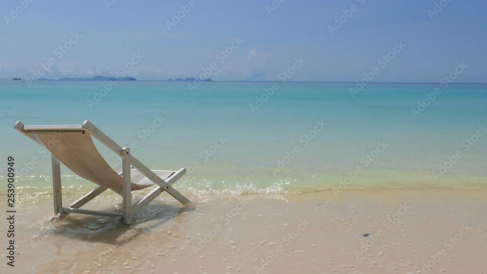 A beach chair getting touched by waves at a paradise beach with white sand and turquoise water. A beach chair getting touched by waves at a paradise beach with white sand and turquoise water.