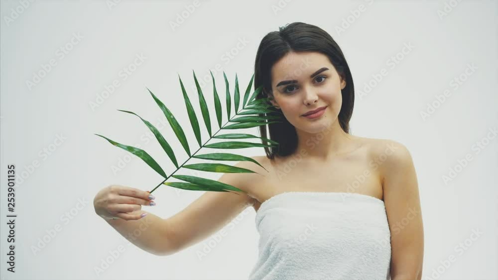 Beautiful young woman with perfect skin and natural make up posing front of plant tropical green leaves background with fern. Young model with wet hair care of her face and body.