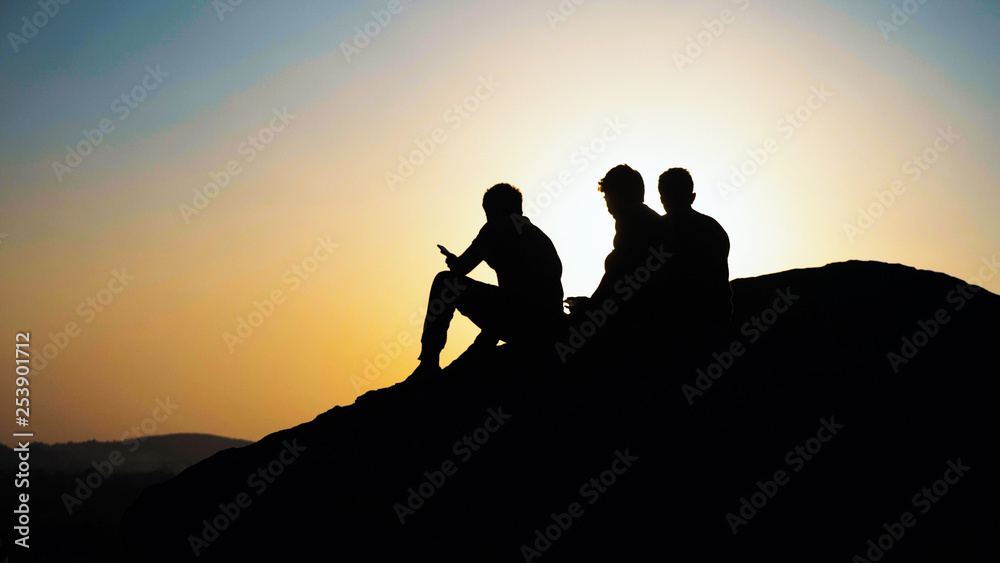 Silhouette of group people sits and admiring the sunset on top of mountain.