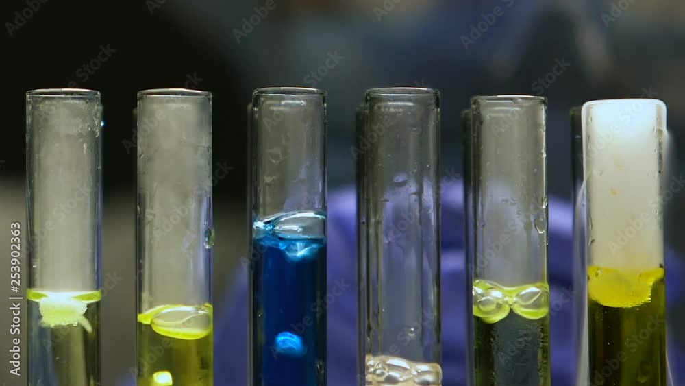 Lab worker adding liquid into test tubes, comparing boiling reaction, production