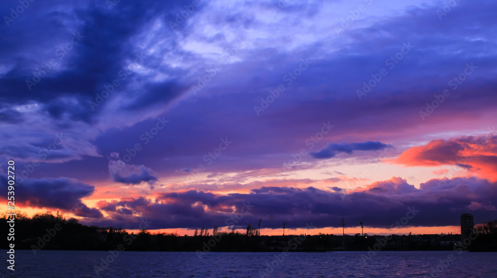 Stormy weather with bright colors in the background over trees at sunset.  Dark and gray cloudy sky over colorful background over the sea