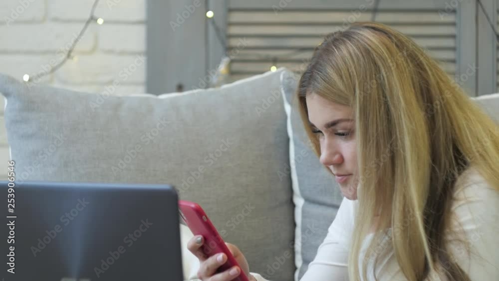 Young woman with smartphone and laptop lying on sofa at home. Young woman with smartphone and laptop lying on sofa at home.