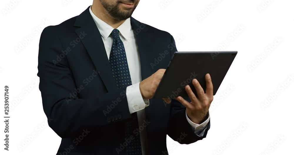Close up of the Caucasian businessman in the suit and tie using tablet computer which holding in his hands on the white wall. Close up of the Caucasian businessman in the suit and tie using tablet computer which holding in his hands on the white wall.