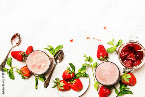 Strawberry dairy smoothies with jam, berry and green mint, white background, top view