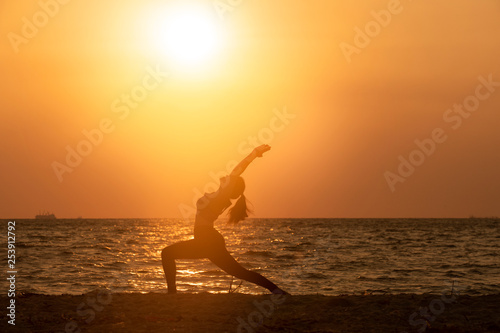 silhouette of woman practicing yoga on the beach at sunset