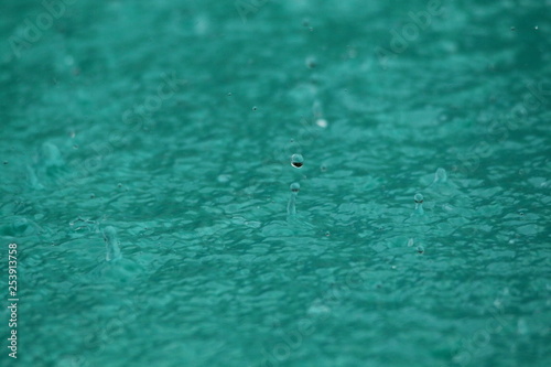 Background photo of rain droplets falling in a pool of water.