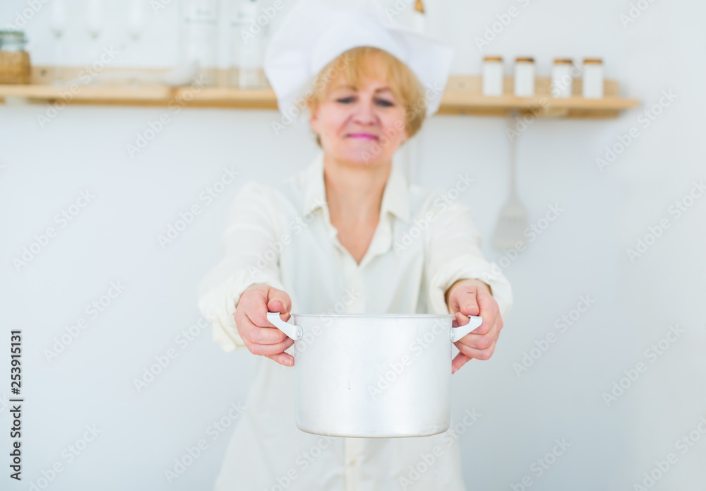 Beautiful senior woman with a wooden pot at home in the kitchen. Selective focus in pan Beautiful senior woman with a wooden pot at home in the kitchen. Selective focus in pan