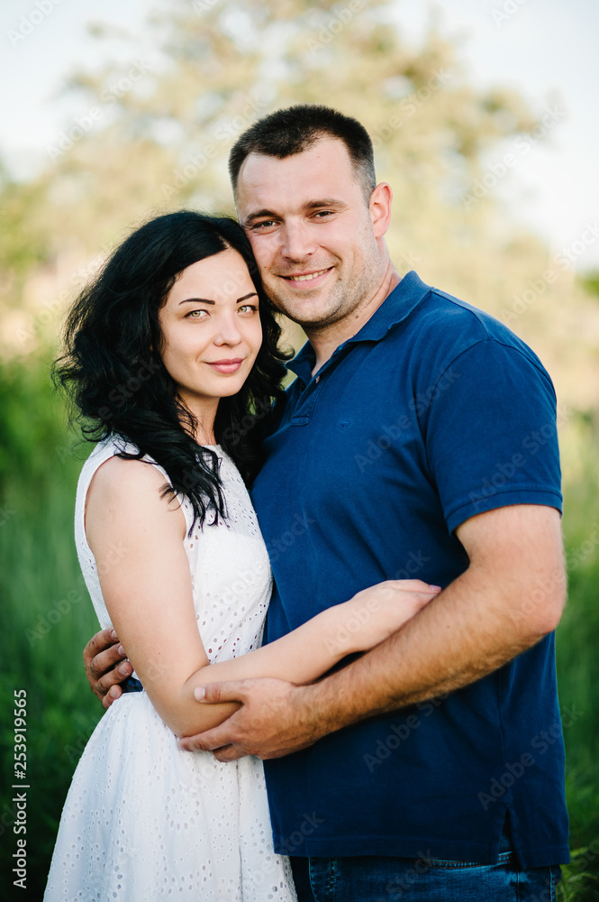 Outdoor shot of young happy couple in love standing on grass in field. Man and woman in sunlight summer park. Happy family in the evening sun light. The concept holiday.
